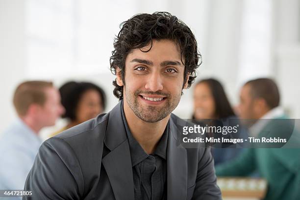 an office in the city. business. team meetings. a group sitting down around a table. one person in the foreground. a man smiling confidently. - cheveux court homme photos et images de collection