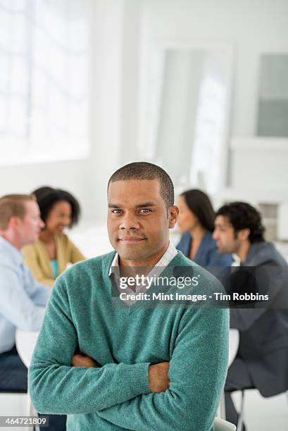an office in the city. business. team meetings. a group sitting down around a table. one person in the foreground. a man smiling confidently. - green shirt stock pictures, royalty-free photos & images