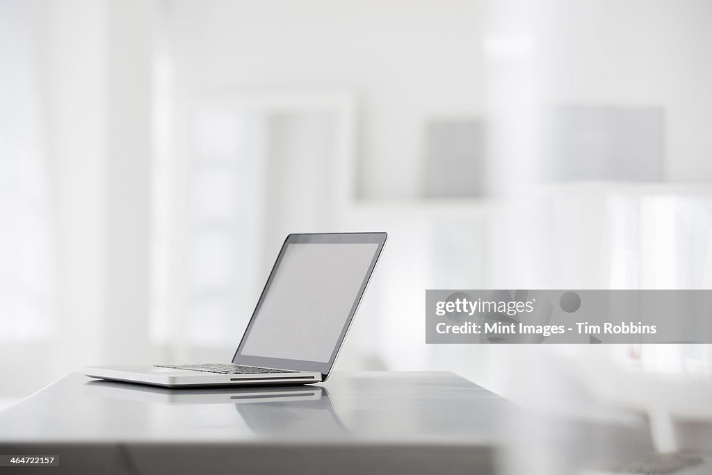 A fresh white building interior, flooded with light. A smooth shiny grey tabletop, and an open laptop computer.