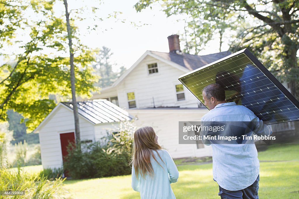 A man carrying a solar panel towards a building under construction.