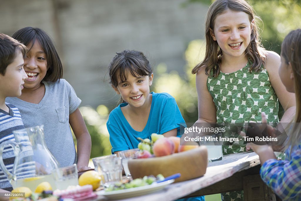 A group of children around a table,eating fresh fruits and salads.