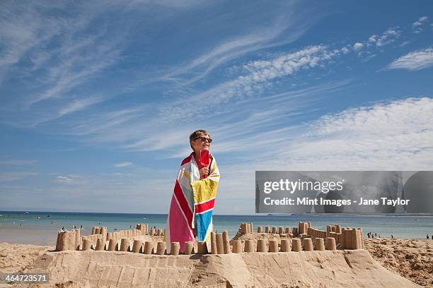 a boy standing beside a sandcastle,on top of a mound of sand. beach. - château de sable photos et images de collection