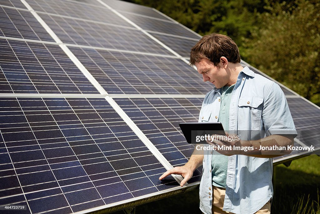 A farmer closely inspecting the surface of a solar panel on the farm.