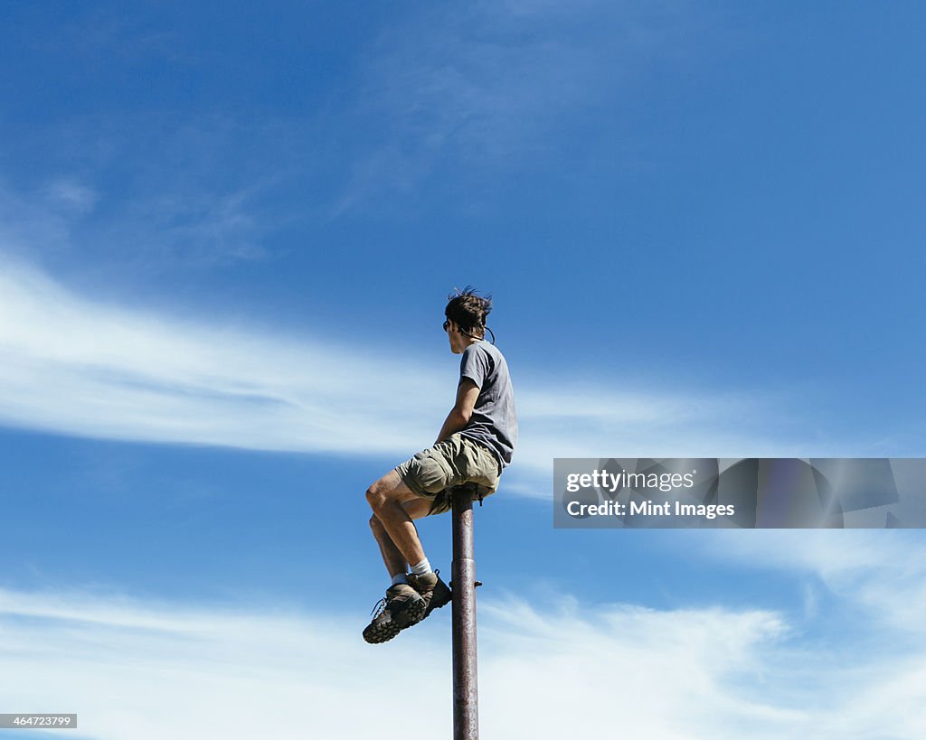 Man sitting and balancing on top of a metal post,looking towards expansive sky,on Surprise Mountain,Alpine Lakes Wilderness,Mt. Baker-Snoqualmie national forest.
