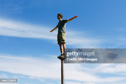 Man standing and balancing on a metal post,looking towards expansive sky,on Surprise Mountain,Alpine Lakes Wilderness,Mt. Baker-Snoqualmie National forest. Man standing and balancing on a metal post,looking towards expansive sky,on Surprise Mountain,Alpine Lakes Wilderness,Mt. Baker-Snoqualmie National forest.