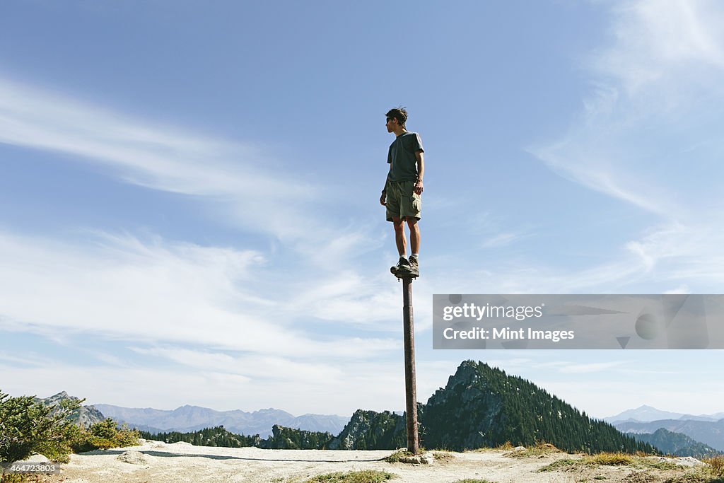 A man standing and balancing on a metal post,looking towards expansive sky,on Surprise Mountain,Alpine Lakes Wilderness,Mt. Baker-Snoqualmie national forest.