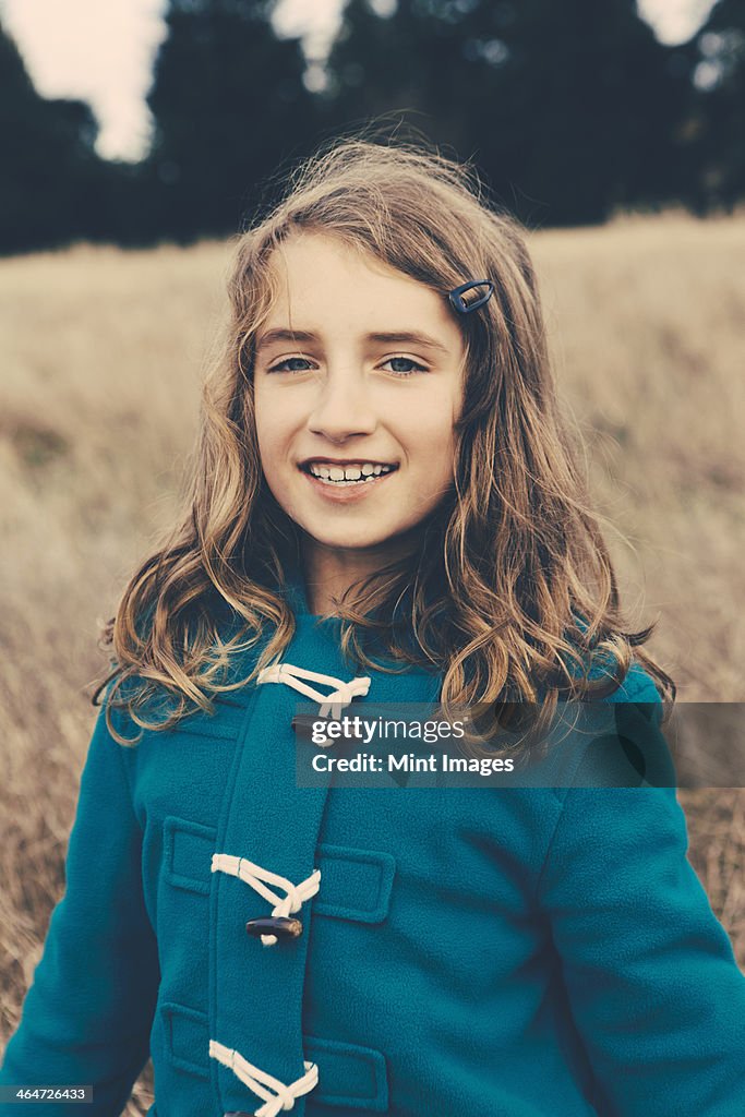 A young girl of nine years old,in a blue duffle coat,smiling at the camera.