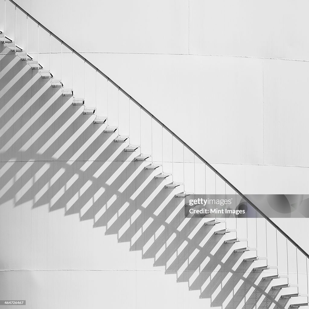 Steps leading up the side of a white storage tank at an oil refinery plant. A pattern of shadows.