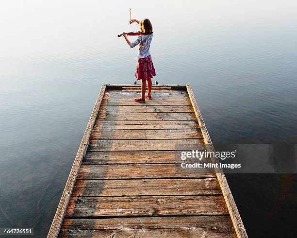 a ten year old girl playing the violin at dawn on a wooden dock. - young violinist stock pictures, royalty-free photos & images