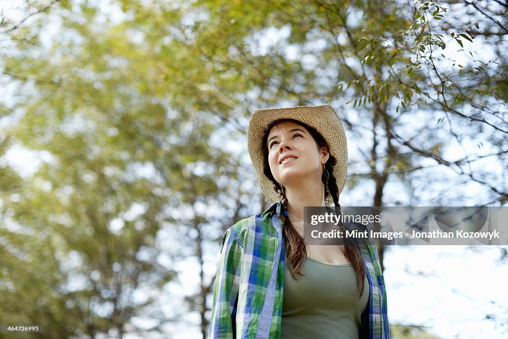 A girl in a straw hat walking in the woods.