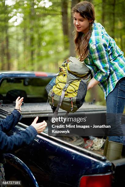 a young woman unloading rucksacks from the back of a pickup truck. - truck side view stock pictures, royalty-free photos & images