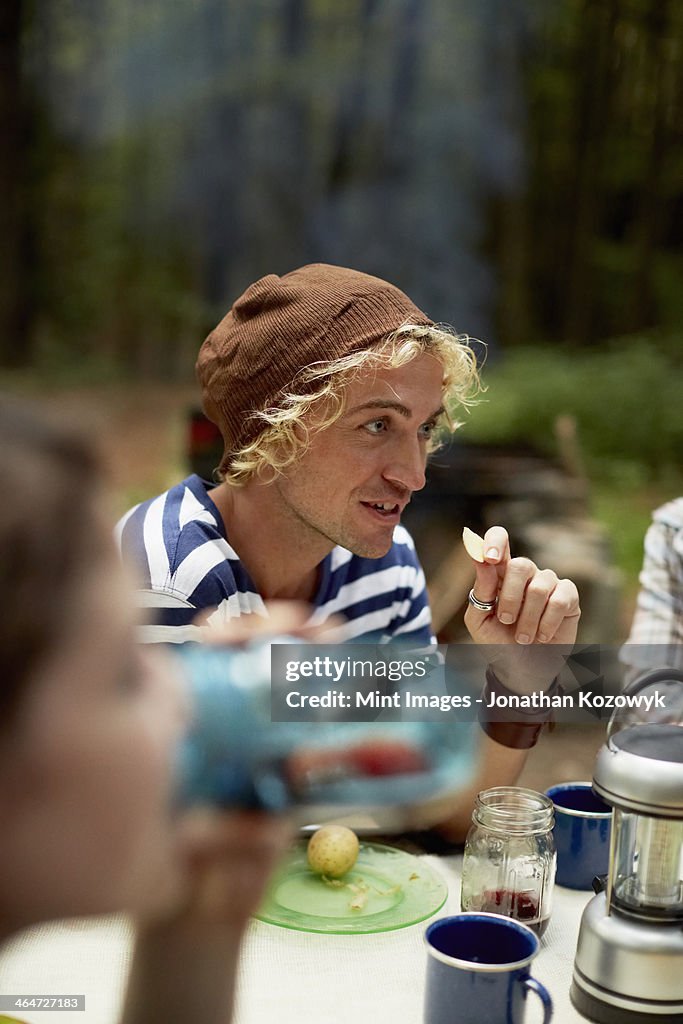 A young man sitting at a picnic table in the woods.