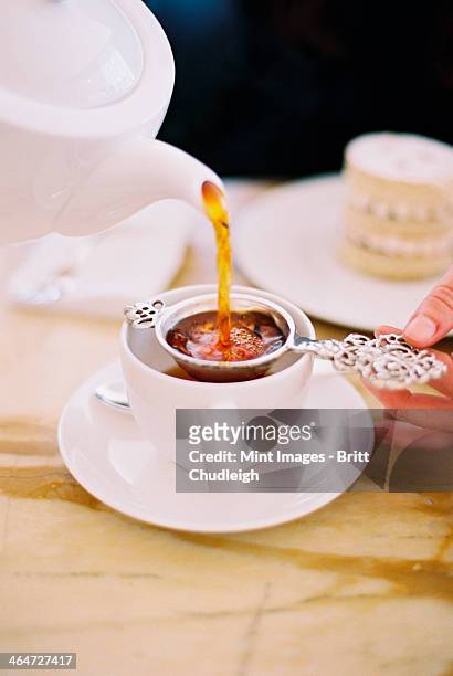 a person pouring a cup of tea, using a strainer. white china. elegant afternoon tea. - teesieb stock-fotos und bilder