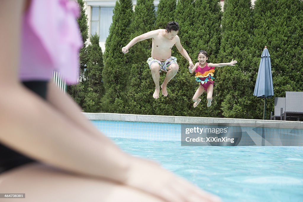 Father and daughter holding hands and jumping into the pool