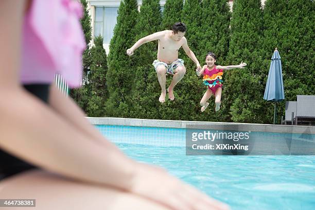 father and daughter holding hands and jumping into the pool - middle age imagens e fotografias de stock