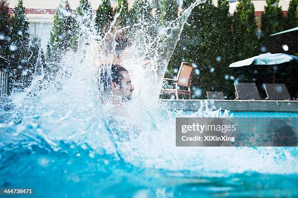 young man jumping into a pool with water splashing all around him - man splashed with colour stock pictures, royalty-free photos & images