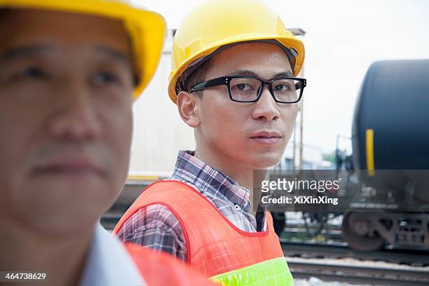 serious engineer in protective workwear looking at camera outside in front of railroad tracks - rail freight stock pictures, royalty-free photos & images