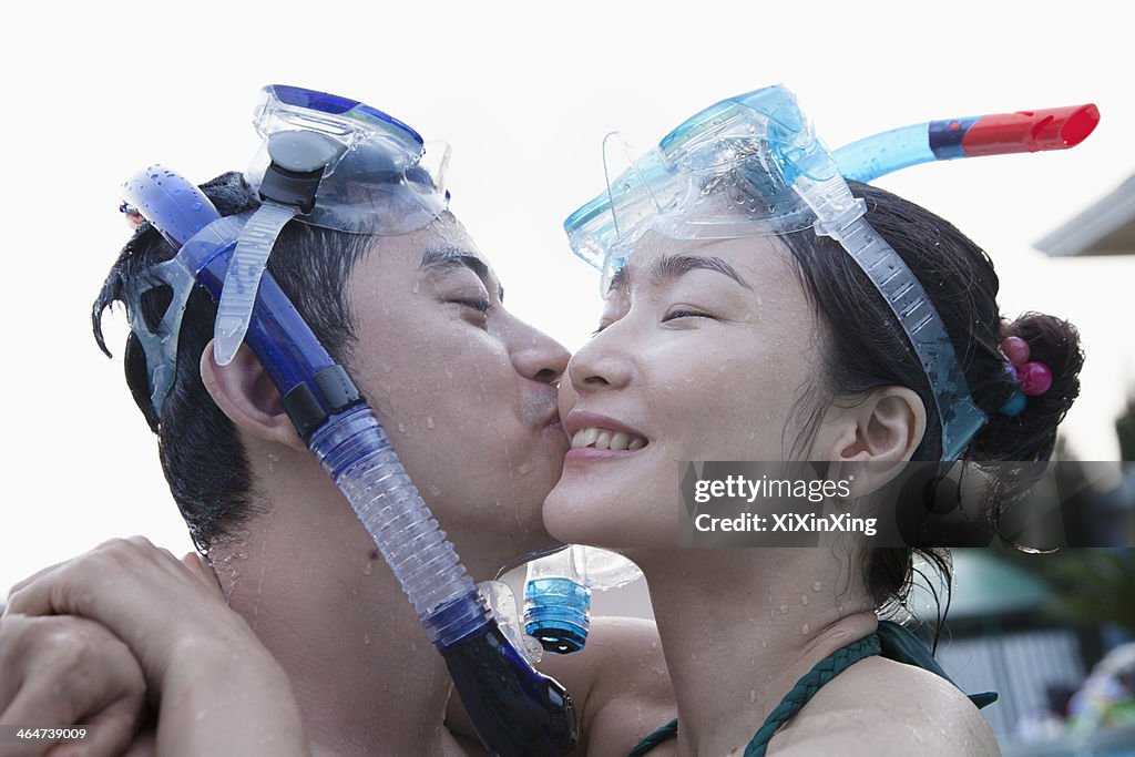 Smiling couple kissing on the cheek wearing snorkeling gear in the pool