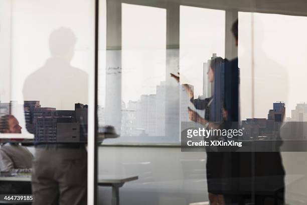 four business people standing and looking at a white board on the other side of a glass wall - woman whiteboard stock pictures, royalty-free photos & images