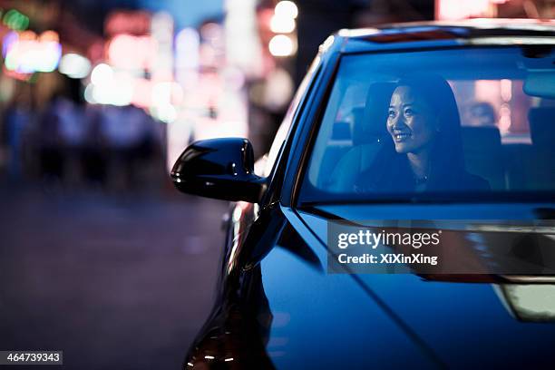 smiling woman looking through car window at the city nightlife - autonomous vehicles stock pictures, royalty-free photos & images