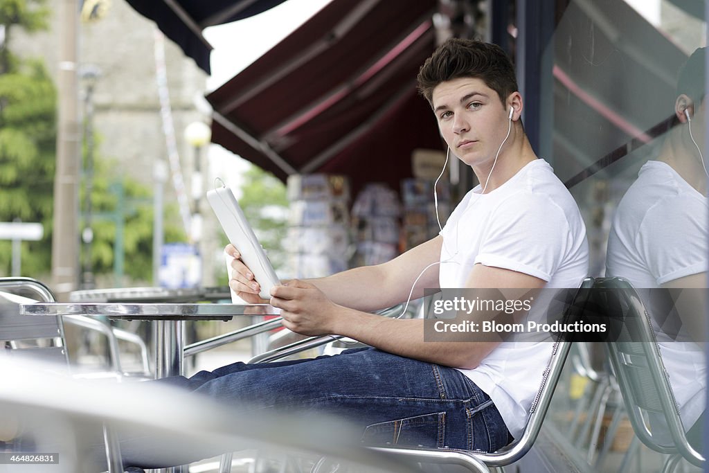 Late teens boy using a tablet outside a cafe