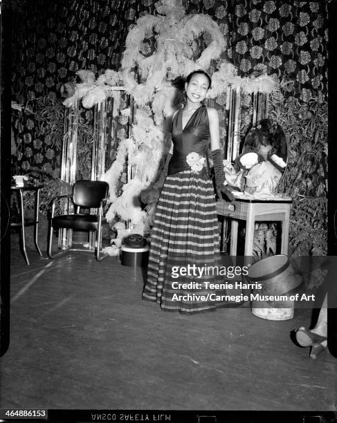 Woman wearing sleeveless gown with striped skirt, posed in Schenley High School with floral curtain, for Beauty Shop Owners' Fashion Review,...