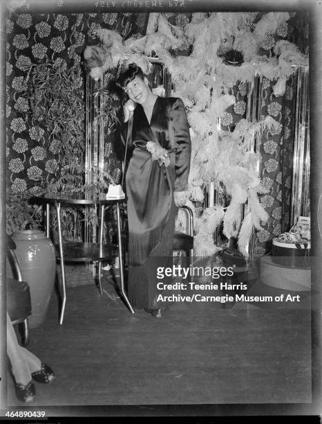 Woman wearing long satin wrap-around dress and holding telephone receiver, against backdrop of floral curtain, feathered decoration, and hydrangeas,...