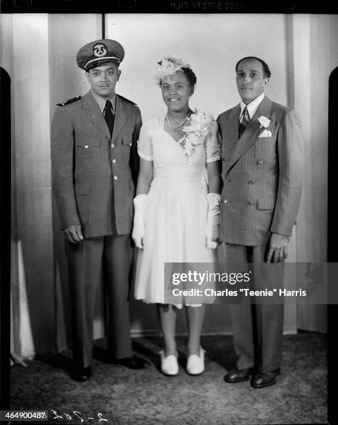 Group portrait of man wearing military uniform, bride Hattie Fordham Banks wearing dress with ruched bodice and sweetheart neckline, and groom...