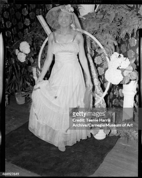 Woman wearing gown and veil in interior with floral curtain, ferns, and hydrangeas in background, for Beauty Shop Owners' Fashion Review in Schenley...