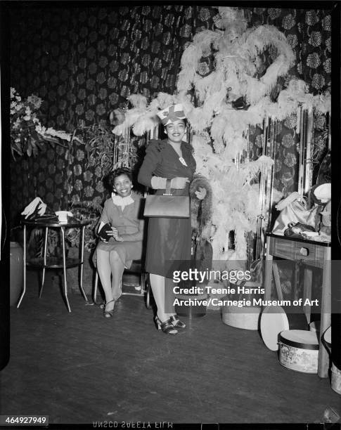 Two women in short dresses gathered in interior with floral curtain and large feathered decoration, for Beauty Shop Owners' Fashion Review in...