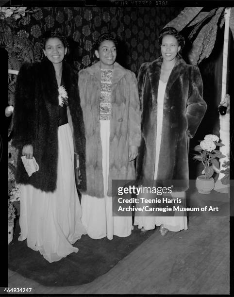 Group portrait of three women wearing long dresses and fur coats in front of floral curtain with hydrangeas, for the Beauty Shop Owners' Fashion...