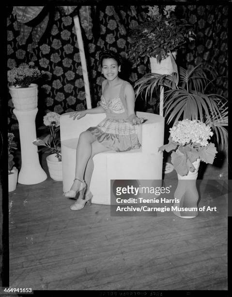 Woman wearing two-piece striped sundress and heels, seated in chair in front of floral curtain, for Beauty Shop Owners' Fashion Review in Schenley...