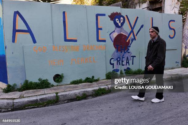 Man walks on March 2, 2015 past a graffito in Athens referring to the Greek Prime Minister Alexis Tsipras, calling him the "Great", and reading "God...