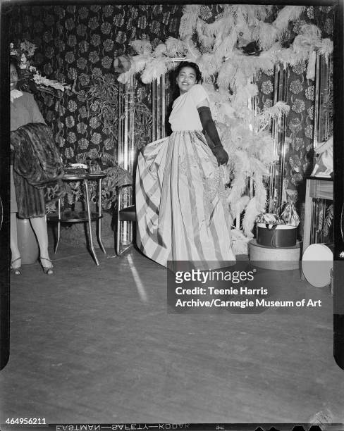 Pocahontas Crews wearing striped skirt with bird design, in interior with floral curtain and large feathered decoration, for Beauty Shop Owners'...