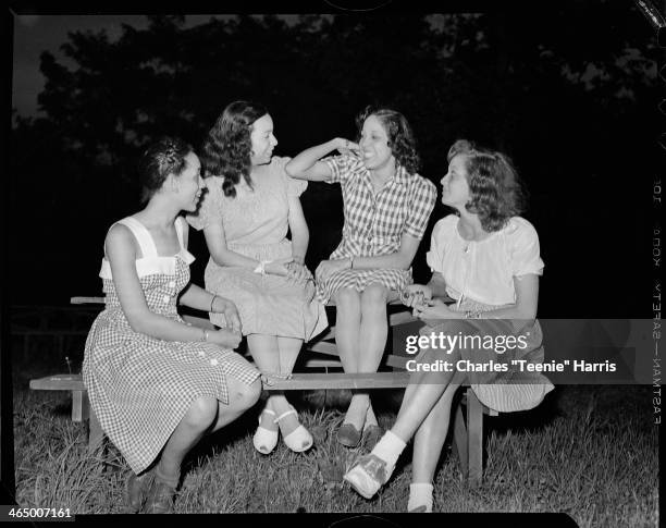 Group portrait of four women, including two wearing gingham dresses, and one on right wearing saddle shoes, gathered around picnic table at North...