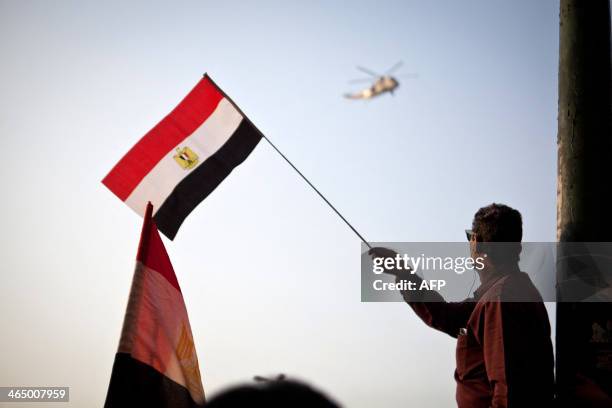 An Egyptian man waves the national flag as an Army helicopter hovers over in Cairo's Tahrir Square during a rally marking the anniversary of the 2011...