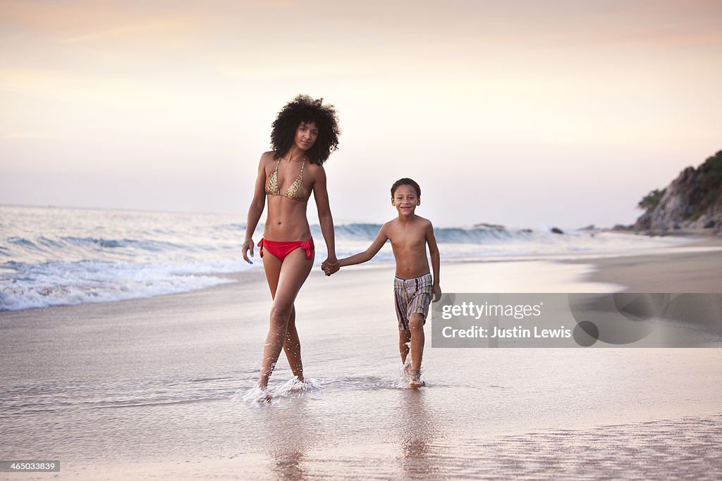 Mother & son walking in sand at beach during sunet