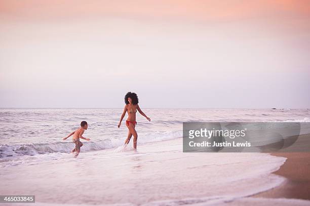 mother and sun running & playing in waves at beach - mother and child in water at beach stock pictures, royalty-free photos & images