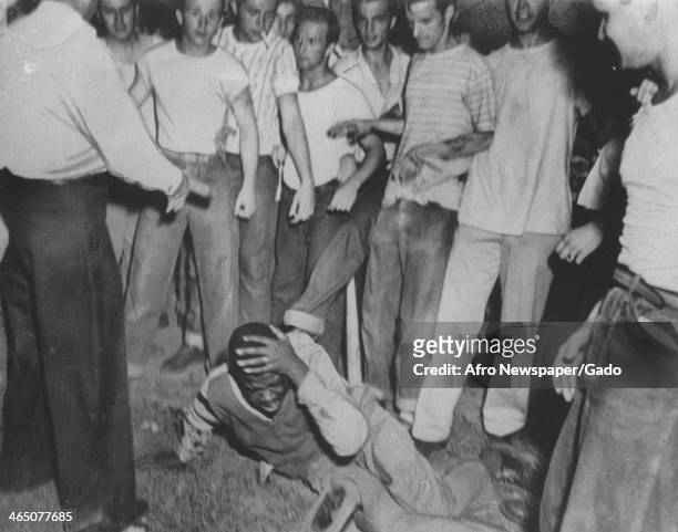 Mob of white teenagers kicks and beats an African American man, who holds his head and screams in pain during a lynching, 1950.