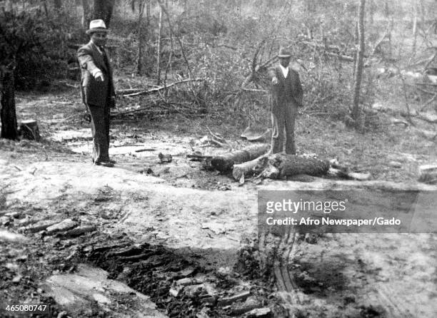 Two African American men point to tire tracks at the scene of a lynching, Georgia, 1930.