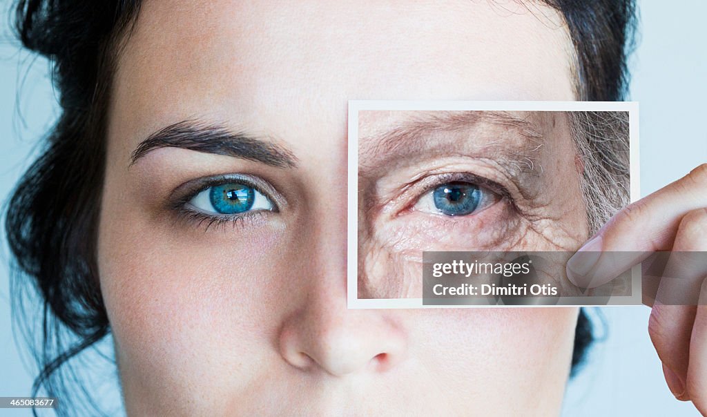 Young woman with photo of aged eye over her own