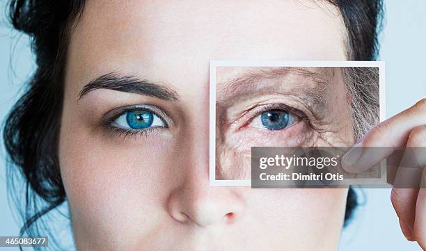 young woman with photo of aged eye over her own - âge humain photos et images de collection