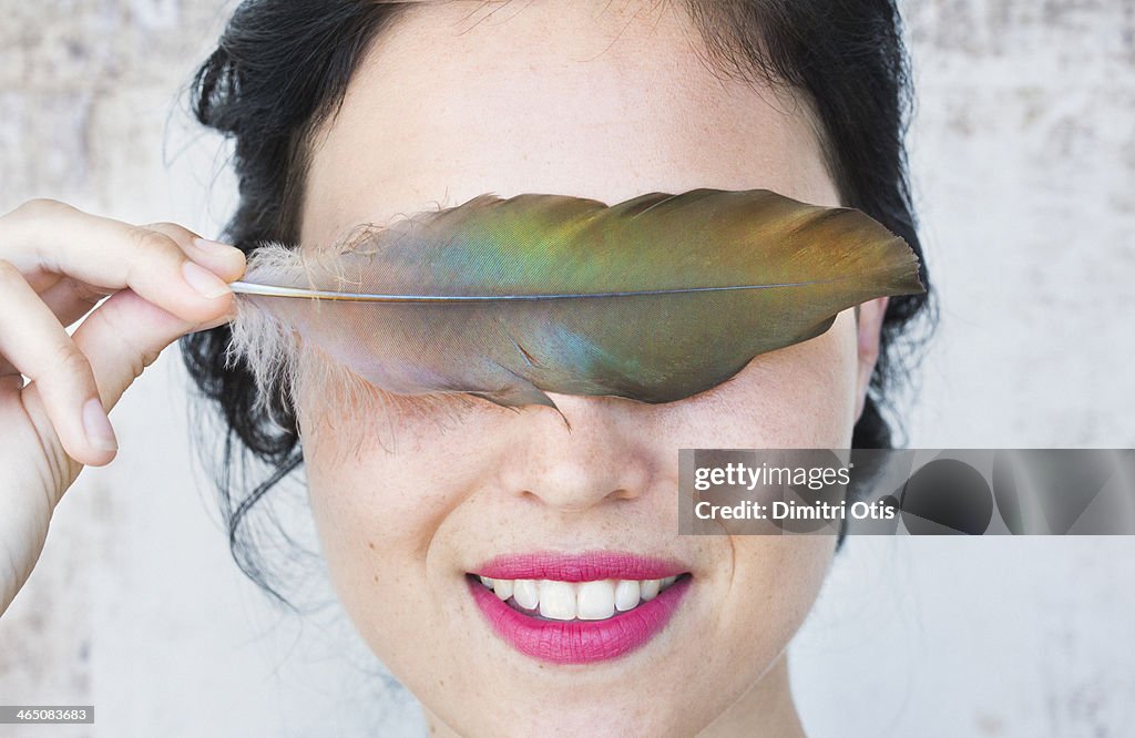 Young woman holding feather over her eyes