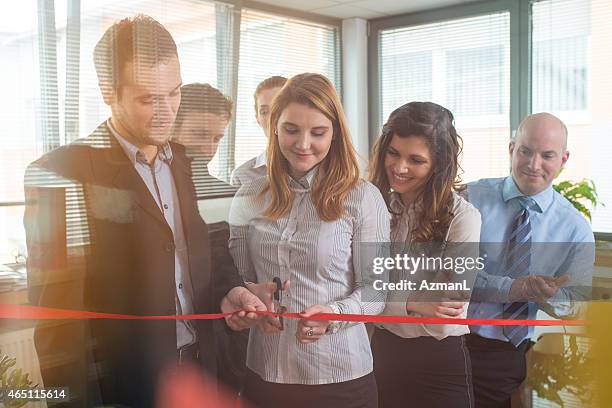 teammates at an office cutting a ribbon for a new beginning - ribbon cutting stock pictures, royalty-free photos & images