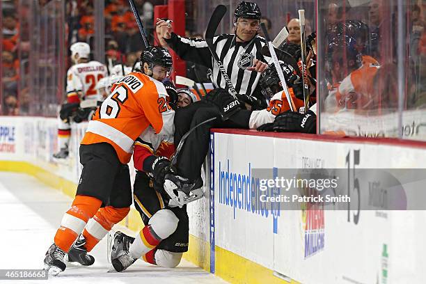 Carlo Colaiacovo of the Philadelphia Flyers hits Josh Jooris of the Calgary Flames as linesmen Scott Driscoll goes over the boards in the first...