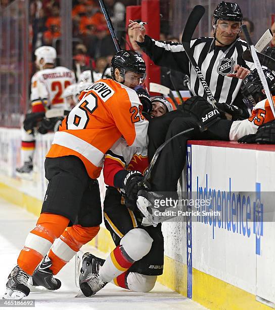 Carlo Colaiacovo of the Philadelphia Flyers hits Josh Jooris of the Calgary Flames as linesmen Scott Driscoll goes over the boards in the first...