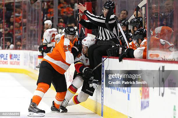 Carlo Colaiacovo of the Philadelphia Flyers hits Josh Jooris of the Calgary Flames as linesmen Scott Driscoll goes over the boards in the first...