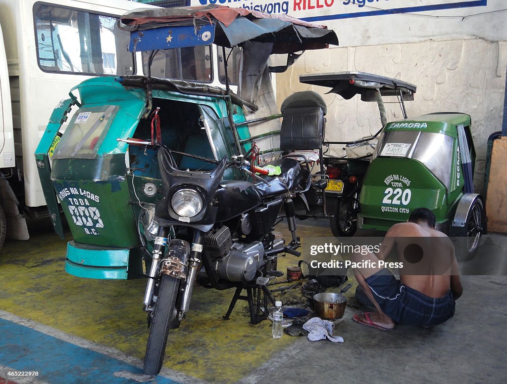 A Filipino man cleans the wheel of a tricycle inside a...