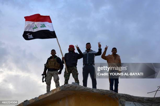 Iraqi government forces and allied militias gesture as they hold the national flag in the northern part of Diyala province, bordering Salaheddin...