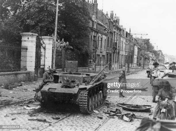 German troops pass a knocked-out German tank as they enter Lille after the siege of the city, France, May-June 1940.